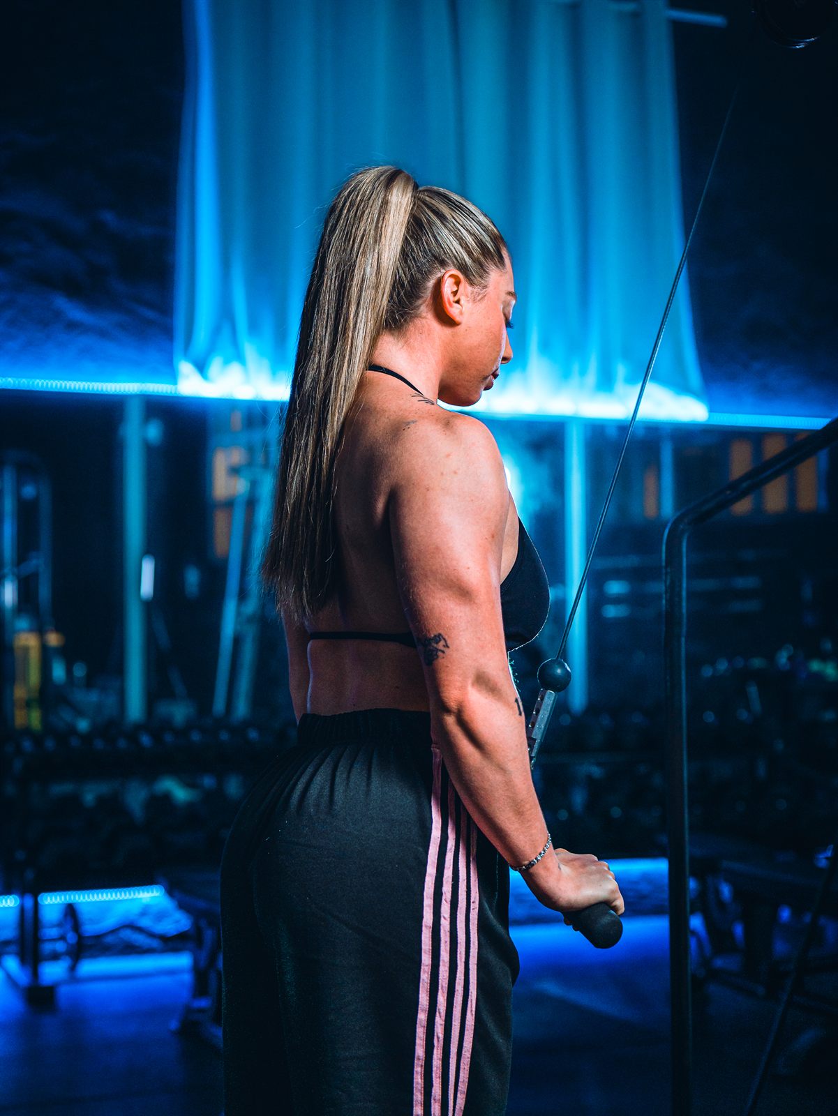 Judith Ramos entrenando en la polea, de espaldas, con las luces azules del gimnasio
