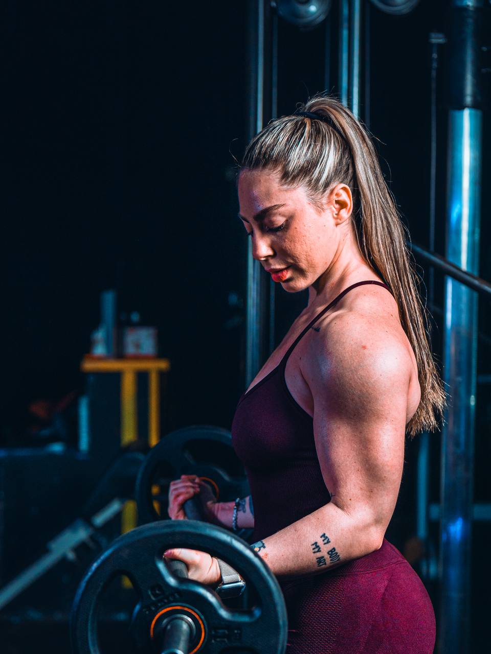 Judith Ramos cargando un disco en la barra, de perfil, en la sala del gimnasio